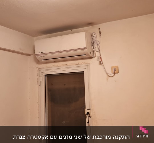 מזגן מותקן על קיר מעל חלון עם כבל חשמל